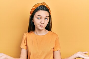 Young brunette girl wearing casual orange t shirt clueless and confused expression with arms and hands raised. doubt concept.