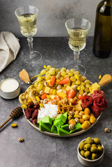 cheese plate with grapes, olives, strawberries, pistachios, meat and two glasses of white wine.