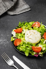 Salad with traditional italian burrata cheese with arugula, lettuce and tomatoes om dark table Top view.
