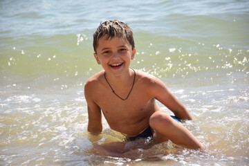 A white race child splashes near the shore on the sea beach and smiles