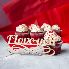 View of red velvet cupcakes and wooden lettering "I love you". Romantic dessert. Square format.