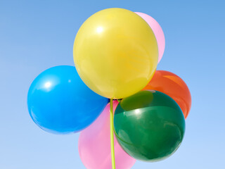Lots of bright colored balloons tied together on a stick close-up against a blue sky. The concept of a holiday, good mood, dreams, success.
