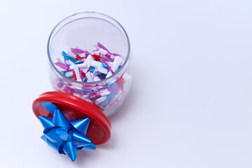 Paper notes with wishes tied with colored ribbons in a glass jar on a table on a white background. Wishes, congratulations, predictions concept. Copy space.