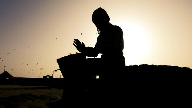 African percussion music, silhouette of a Senegalese man playing a traditional djembe drum with his hands at sunset. Outdoor music at the beach of Essaouira, Morocco. 4k
