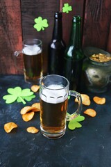 Patrick Day, foamy beer in glass mugs and a bottle, chips, golden coins and a green shamrock on a wooden background, party, congratulation, postcard