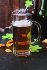 Patrick Day, foamy beer in glass mugs and a bottle, chips, golden coins and a green shamrock on a wooden background, party, congratulation, postcard