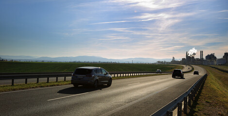 Samochody na drodze szybkiego ruchu, krajobraz wiejski przed zachodem słońca, fabryka, zakład.