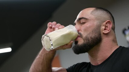 active strong young bearded male athlete drinking milk protein gainer from glass indoors - Powered by Adobe