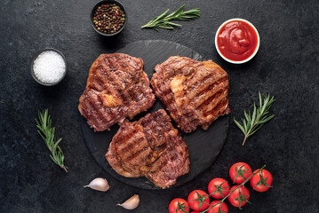 three grilled beef steaks with spices on a stone background