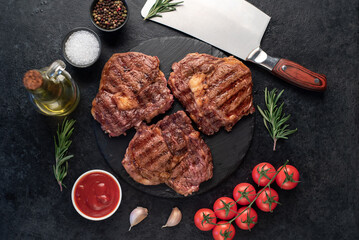 three grilled beef steaks with spices on a stone background