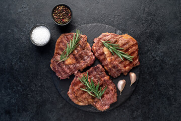 three grilled beef steaks with spices on a stone background