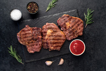 three grilled beef steaks with spices on a stone background