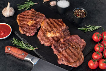 three grilled beef steaks with spices on a stone background