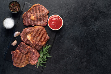 three grilled beef steaks with spices on a stone background with copy space for your text
