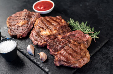three grilled beef steaks with spices on a stone background