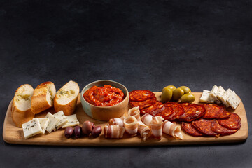 Charcuterie and cheese plate on wooden board on black background. Serbian meze - kulen sausage, balkan bacon, goat cheese, olives and ajvar sauce. Copy space.