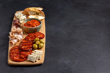 Charcuterie and cheese plate on wooden board on black background. Serbian meze - kulen sausage, balkan bacon, goat cheese, olives and ajvar sauce. Copy space.