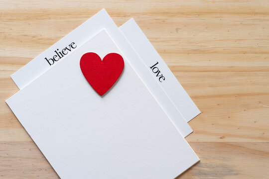 isolated wooden heart painted red on a set of cards with the words "believe" and "love" on a wooden surface