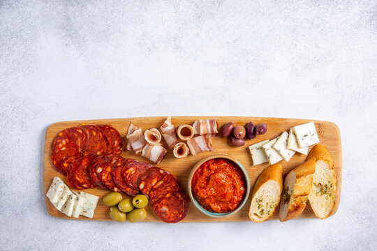 Charcuterie and cheese plate on wooden board on gray background. Serbian meze - kulen sausage, balkan bacon, goat cheese, olives and ajvar sauce. Top view, copy space.