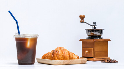 ice americano coffee in a cup with croissant on wooden plate and coffee bean grinder