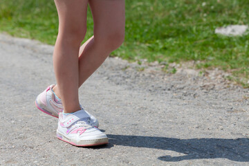 Anonymous unrecognizable elementary school age child walking down the road wearing generic velcro sport shoes legs closeup, one person, summer outdoors scene. Leisure, parks, outdoor activity footwear