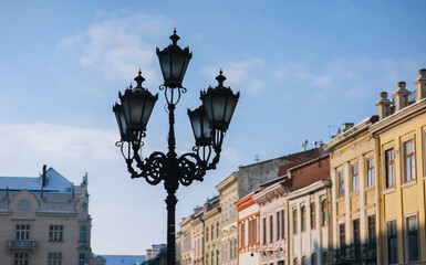 Fototapeta na wymiar An old black vintage lantern in the historical center of Lviv (Rynok Square) on blue sky background. The concept of spring city.