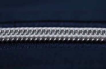 Close-up of a silver plastic zipper closed in the middle of a blue fabric texture