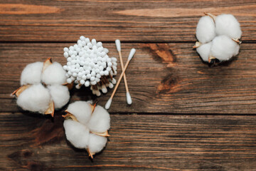 Cosmetic eco sticks on a cardboard base are scattered with cotton on a wooden background.