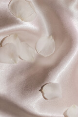 White rose petals on a silk beige background, space for text.