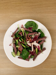 Fresh salad with meat, herbs and pomegranate on white plate on wooden table