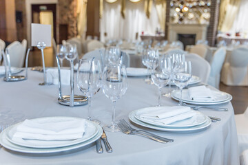 a table with a clean white tablecloth served with plates and glasses empty in the hall before the arrival of guests