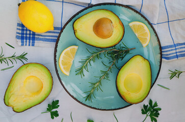 Slices of fresh avocado with herbs and lemons lies on the table on a blue plate. Flat lay. Top view. Healthy food concept. Diet. Vegan. 