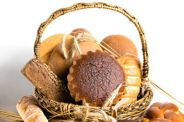 Assorted bread and sweet buns in a basket with spikelets of wheat on a white background