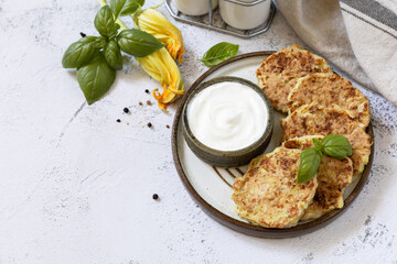 Zucchini fritters. Vegetarian zucchini pancakes with cheese, served with sour cream on a rustic wooden table. Healthy food, low calories keto dieting meal. Copy space.