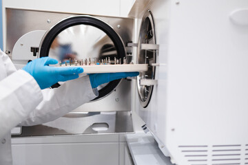 Close-up view of the hands of female dentistry worker who puts a dental instrument into autoclave. Sterilization of medical equipment