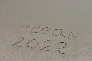 The inscription ocean 2022 on the sand by the water and the rising wave, seashore beach vacation by the sea