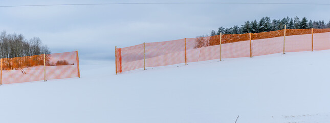 Orange perforated plastic foil barriers against snow in farmland. This protects the snow cover on...