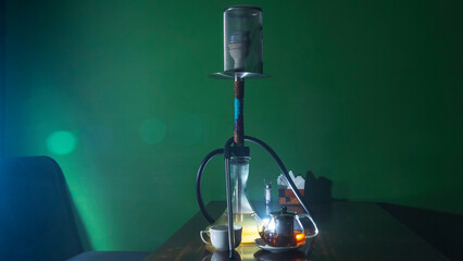 Traditional Arabian shisha and tea with lens flare. A pot of tea and Smoking hookah on a dark green background.