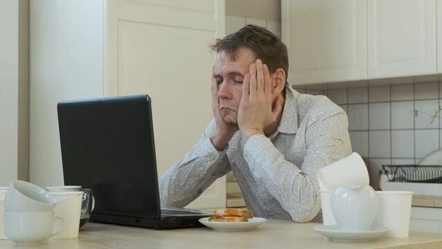 Exhausted Man Drinking from Coffee Pot while Using Laptop at Home. Lots of Empty Coffee Cups Scattered All Over the Table. Working Overtime, Remote Work and Freelancer Lifestyle Concept