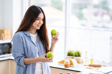 Young pretty Asian women choose fruit and apple for her breakfast inside of the kitchen. Good food with nutrition for healthy eating or diet for weight control.