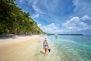 Vacation on the seashore. Back view of young woman walking away on the beautiful tropical white sand beach.