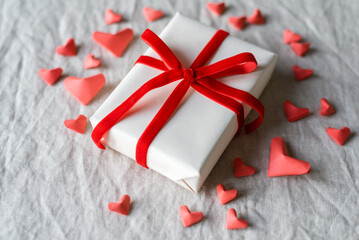 A beautifully wrapped valentine's gift decorated with red ribbon and surrounded by red hearts.
