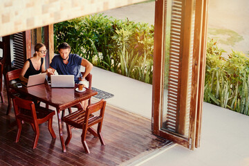 Coworking and freelance concept. Young  bearded man  and young woman working together on laptop computers while sitting on cafe terrace.