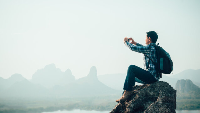 Smart traveler man taking photo by smartphone with beautiful sunset from top of the mountain.Concept of adventure travel