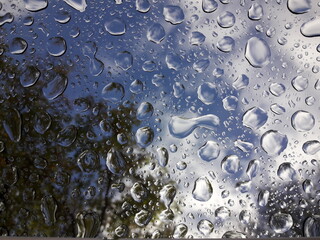 Blick nach oben zum wolkigen Himmel durch ein Fenster mit großen einzigartigen Wassertropfen. Gutes Themenbild für Wetter, Klimawandel