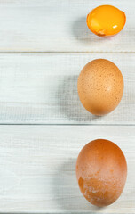 Fresh chicken eggs. Two whole brown chicken eggs and one cracked on a white wooden background. Yolk and two eggs vertically, copy space, selective focus
