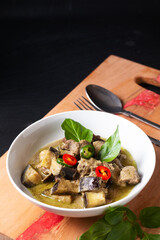 Thai Food concept homemade Thai Green curry in white ceramic bowl on wooden board and black slate stone background with copy space