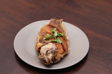 The fried tilapia was just right. Served in gray work on a brown wooden table.