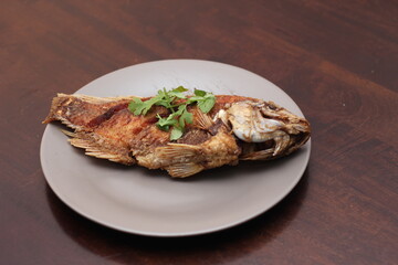 The fried tilapia was just right. Served in gray work on a brown wooden table.