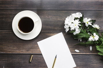 White blank sheet with a bouquet of chrysanthemums and a cup of coffee on a wooden table. Celebration.